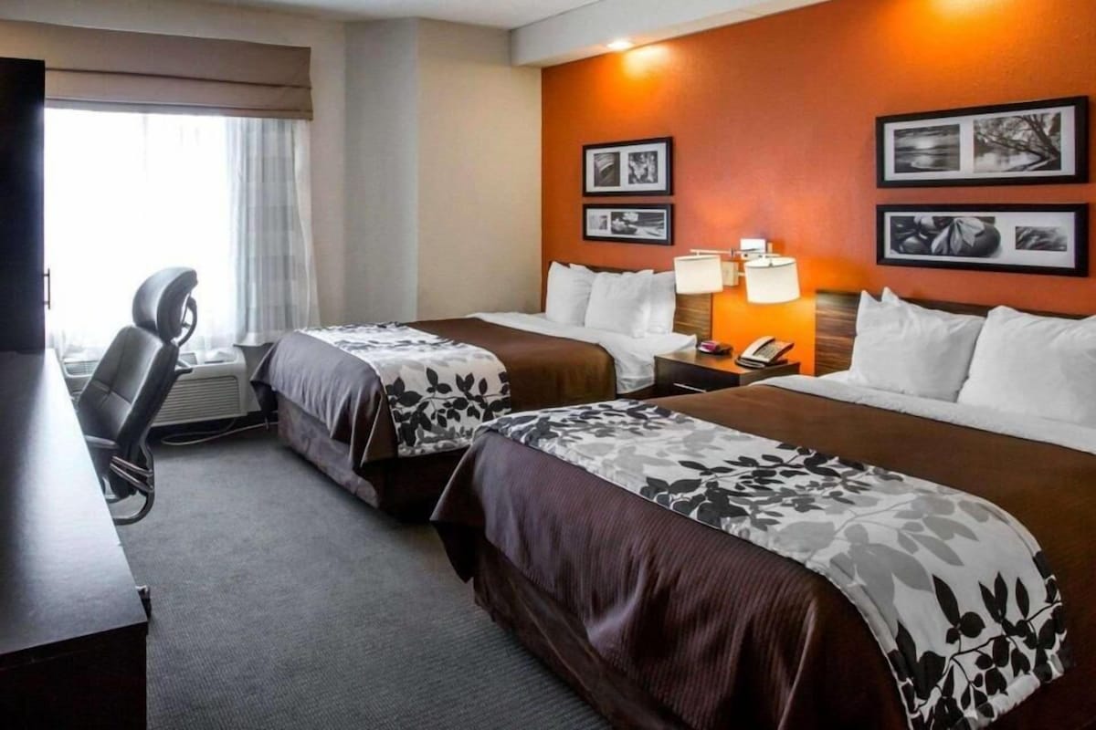A hotel room with two beds, a desk, a chair, and a window.