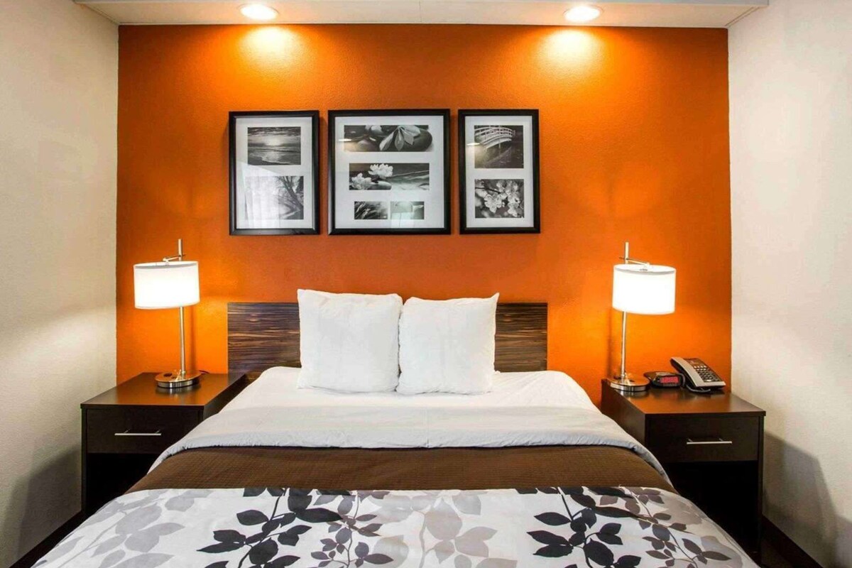 A hotel room with a bed, two bedside tables, a nightstand, and three framed pictures on the wall.