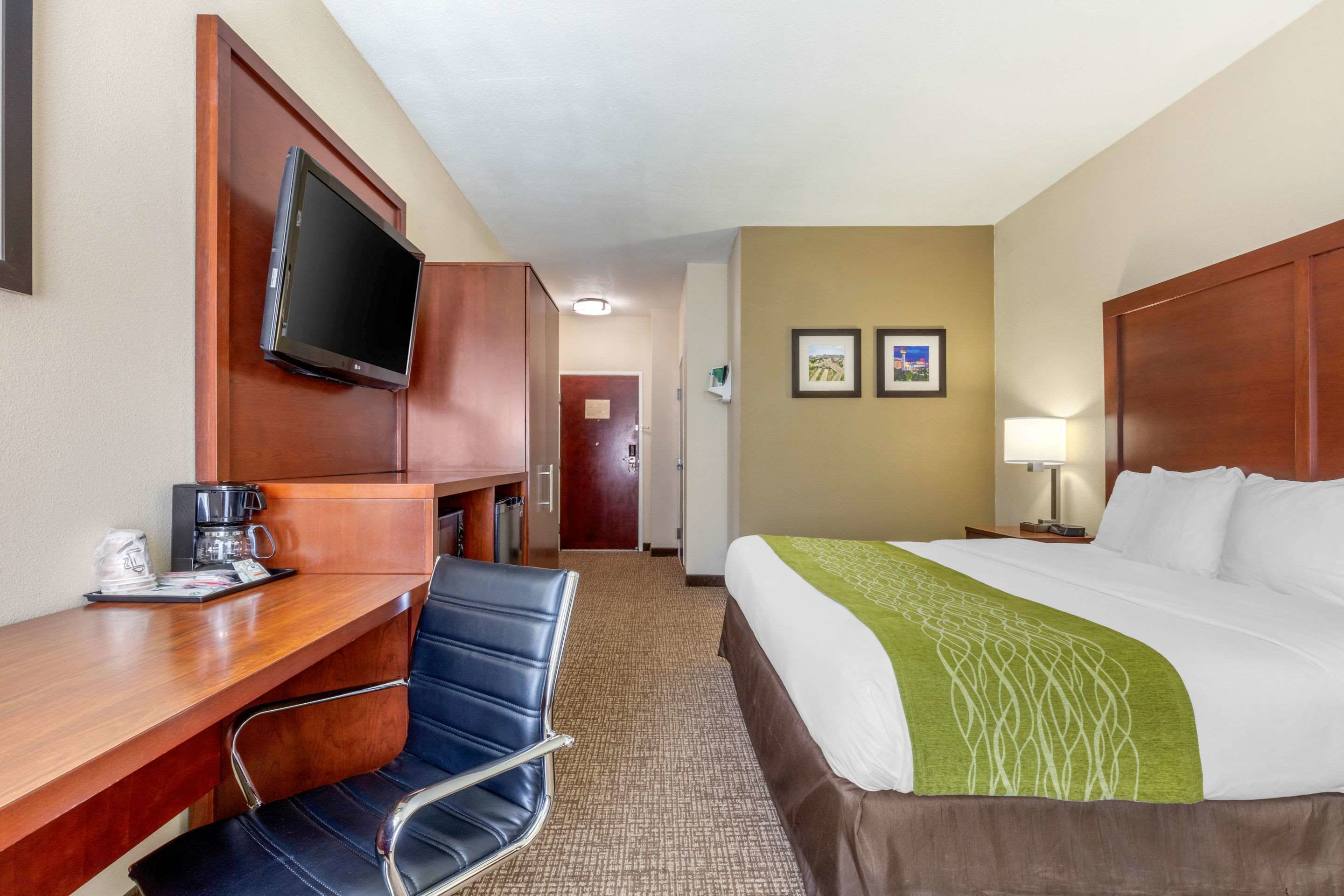 A hotel room with a bed, a desk with a chair, a television, and two framed pictures on the wall.