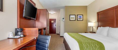 A hotel room with a bed, a desk with a chair, a television, and two framed pictures on the wall.