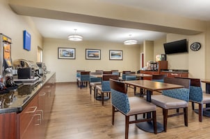 Un comedor de hotel con mesas y sillas de madera, una máquina de café y cuadros en la pared.