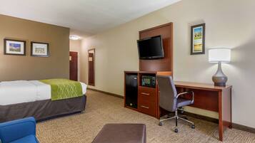 A hotel room with a bed, a desk, a chair, a TV, and a lamp.