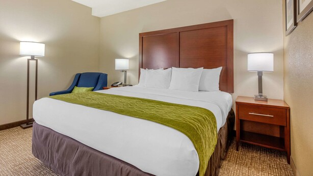 A hotel room with a large bed, a chair, a nightstand, and two lamps.