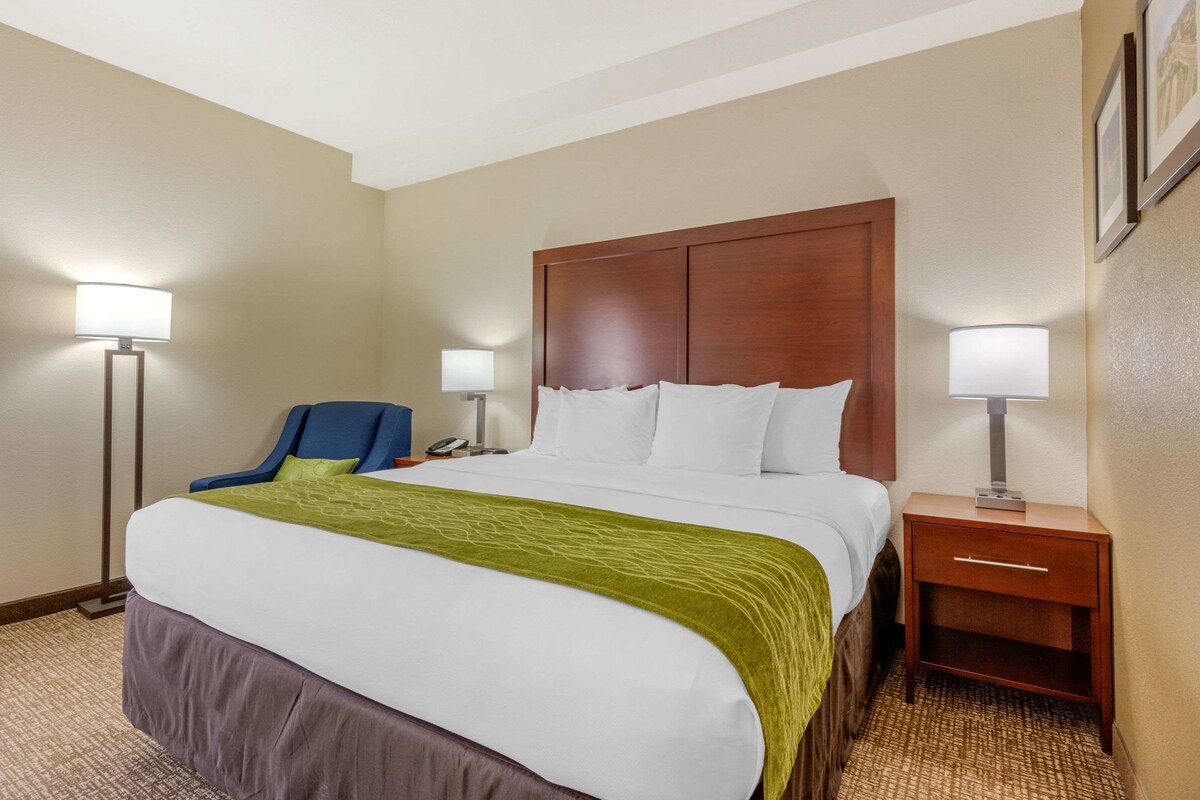 A hotel room with a large bed, a chair, a nightstand, and two lamps.