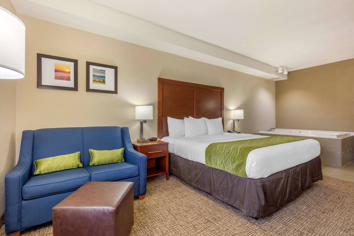 Une chambre d’hôtel avec un lit, un canapé bleu, une table de chevet, une lampe et une salle de bain avec une baignoire.