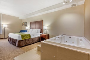 A hotel room with a bed, bedside table, lamp, and a separate bathroom with a bathtub.