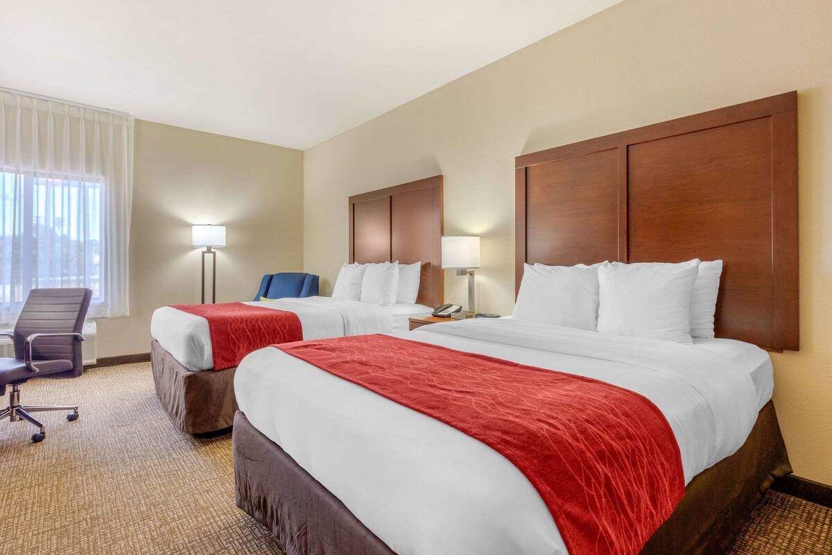 Une chambre d’hôtel avec deux lits, un bureau, une chaise et une lampe.