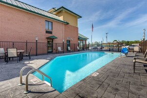 Zona de piscina con un edificio de ladrillo, sillas de descanso y una bandera.