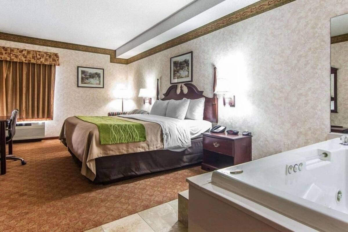 Une chambre d’hôtel avec un lit, une table de chevet, une lampe et une baignoire.