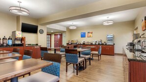 A hotel dining area with multiple tables and chairs, a coffee machine, and a television mounted on the wall.