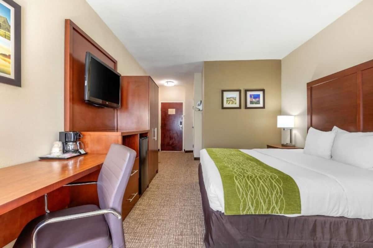 Une chambre d’hôtel équipée d’un lit, d’un bureau, d’une chaise, d’une télévision et d’œuvres d’art accrochées au mur.