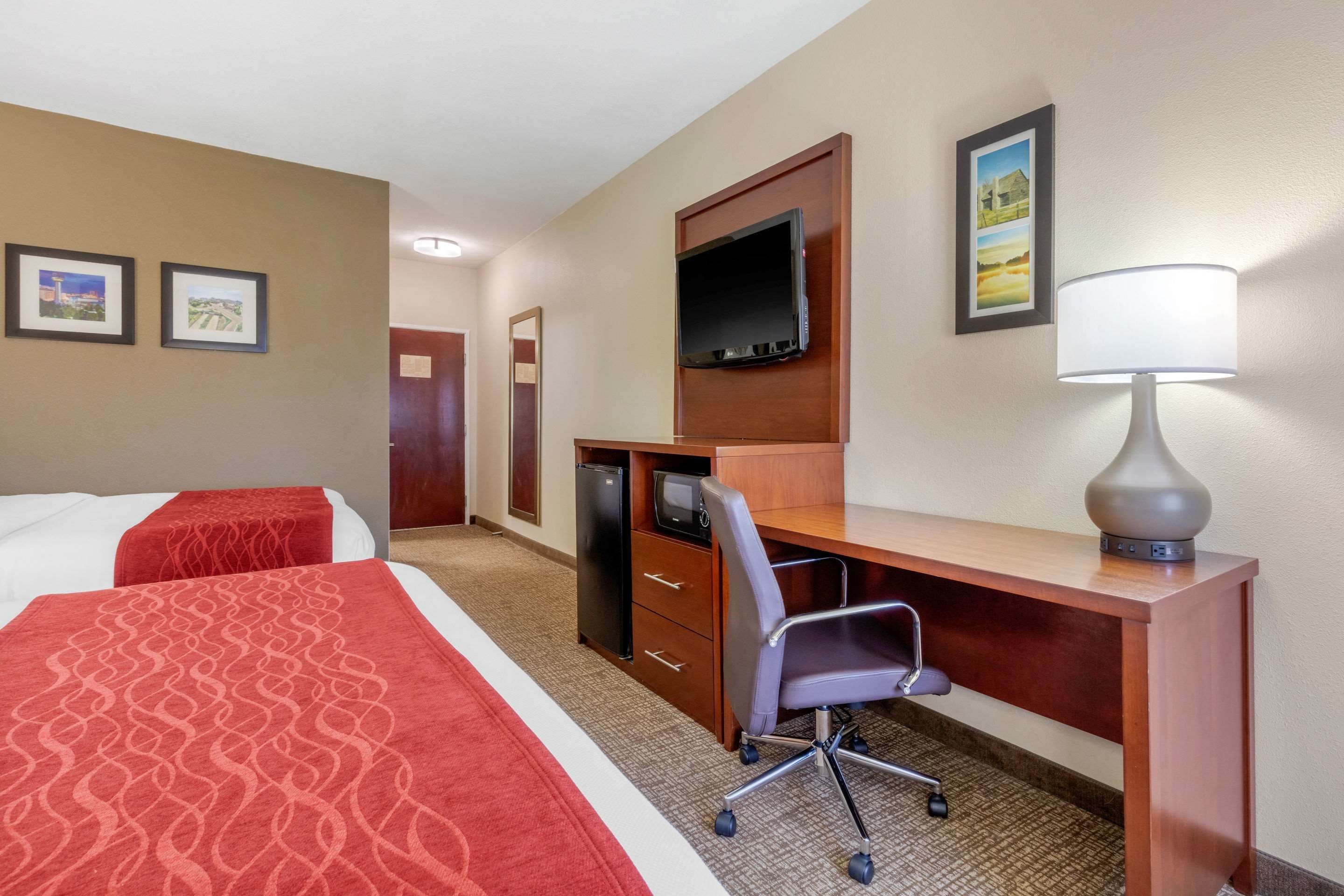 Une chambre d’hôtel avec deux lits, un bureau avec une chaise, une télévision et une lampe.