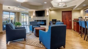 A modern hotel lobby with a fireplace, comfortable seating, a bar area, and a large TV screen.