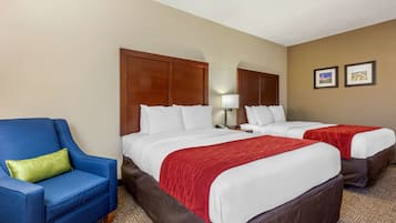 Una habitación de hotel con dos camas, un sillón azul y una manta roja.