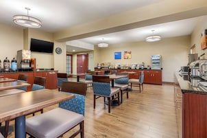 A hotel dining area with multiple tables and chairs, a coffee station, and a television mounted on the wall.