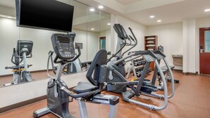 A gym with cardio machines, a mirrored wall, and a television.