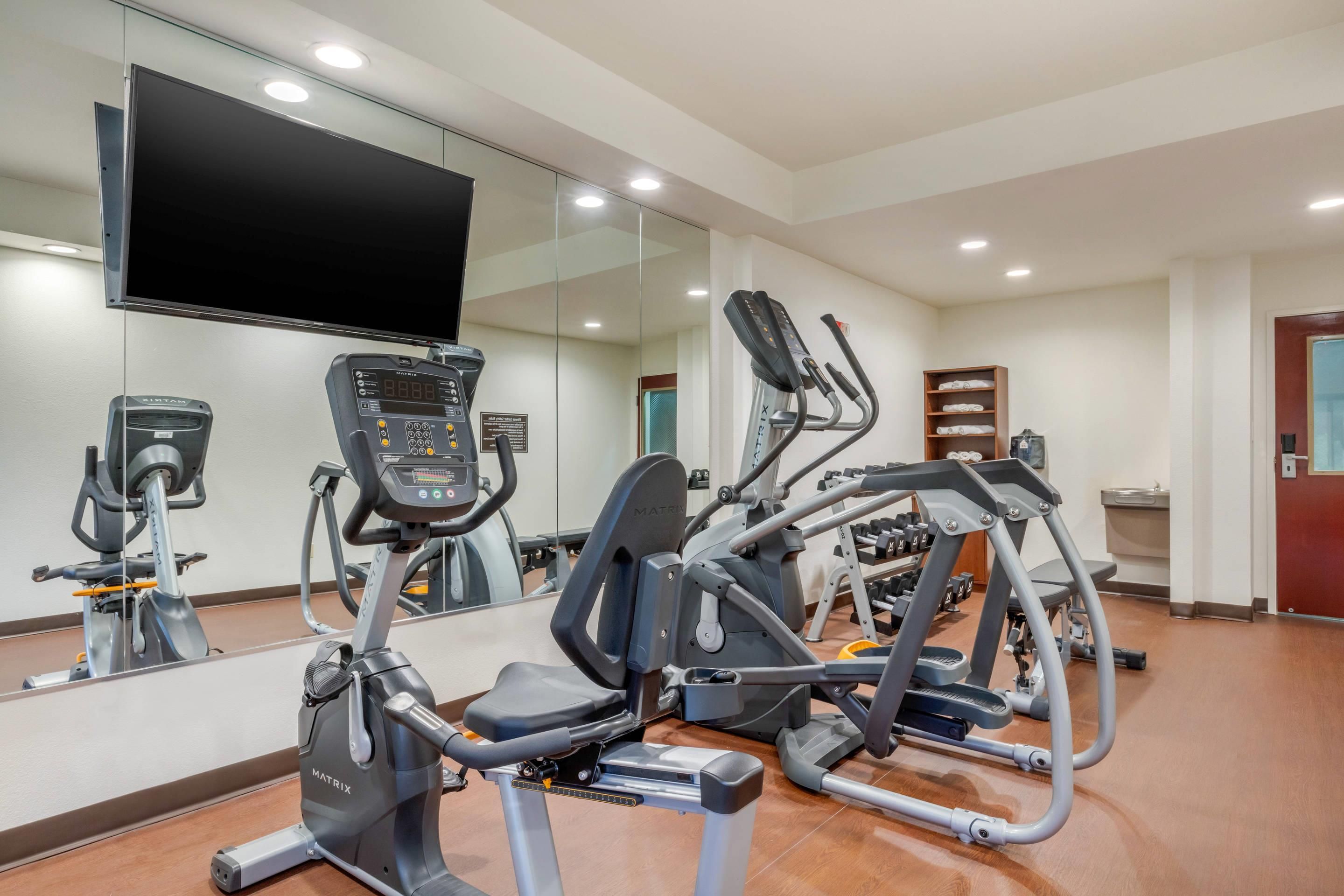 Un gimnasio con equipos de ejercicio variados, incluyendo cintas de correr y una máquina elíptica.