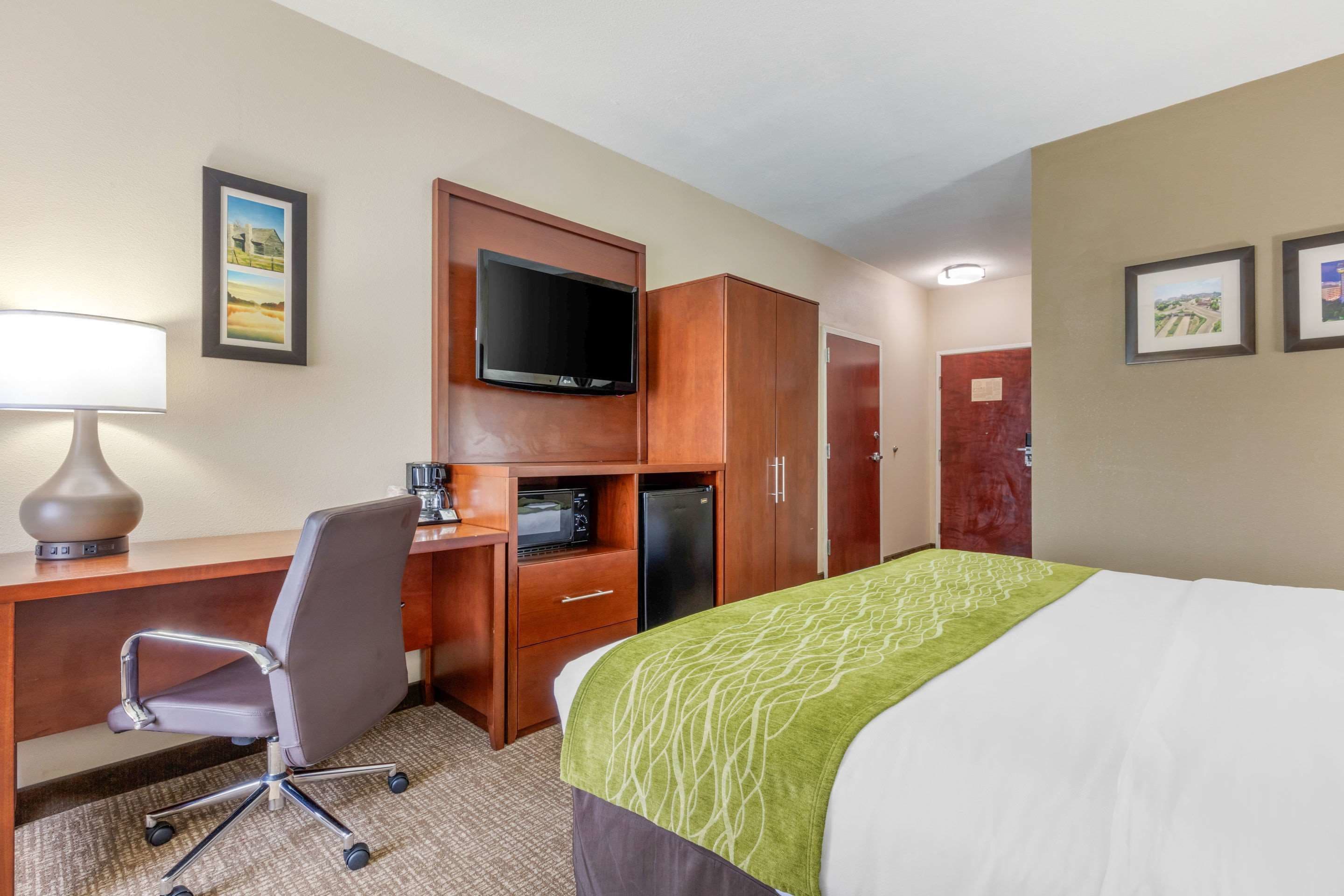 Una habitación de hotel con cama, escritorio con silla, televisor y microondas.