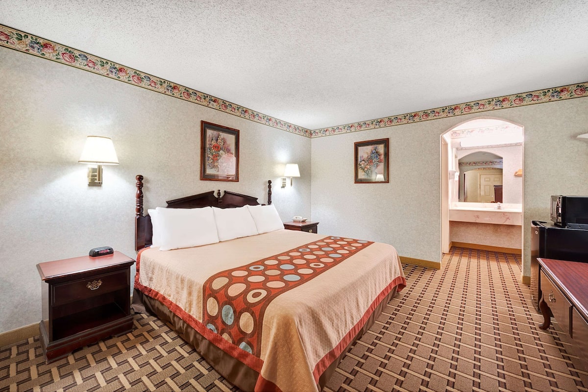 Una habitación de hotel con una cama, mesitas de noche, lámparas y una alfombra estampada.