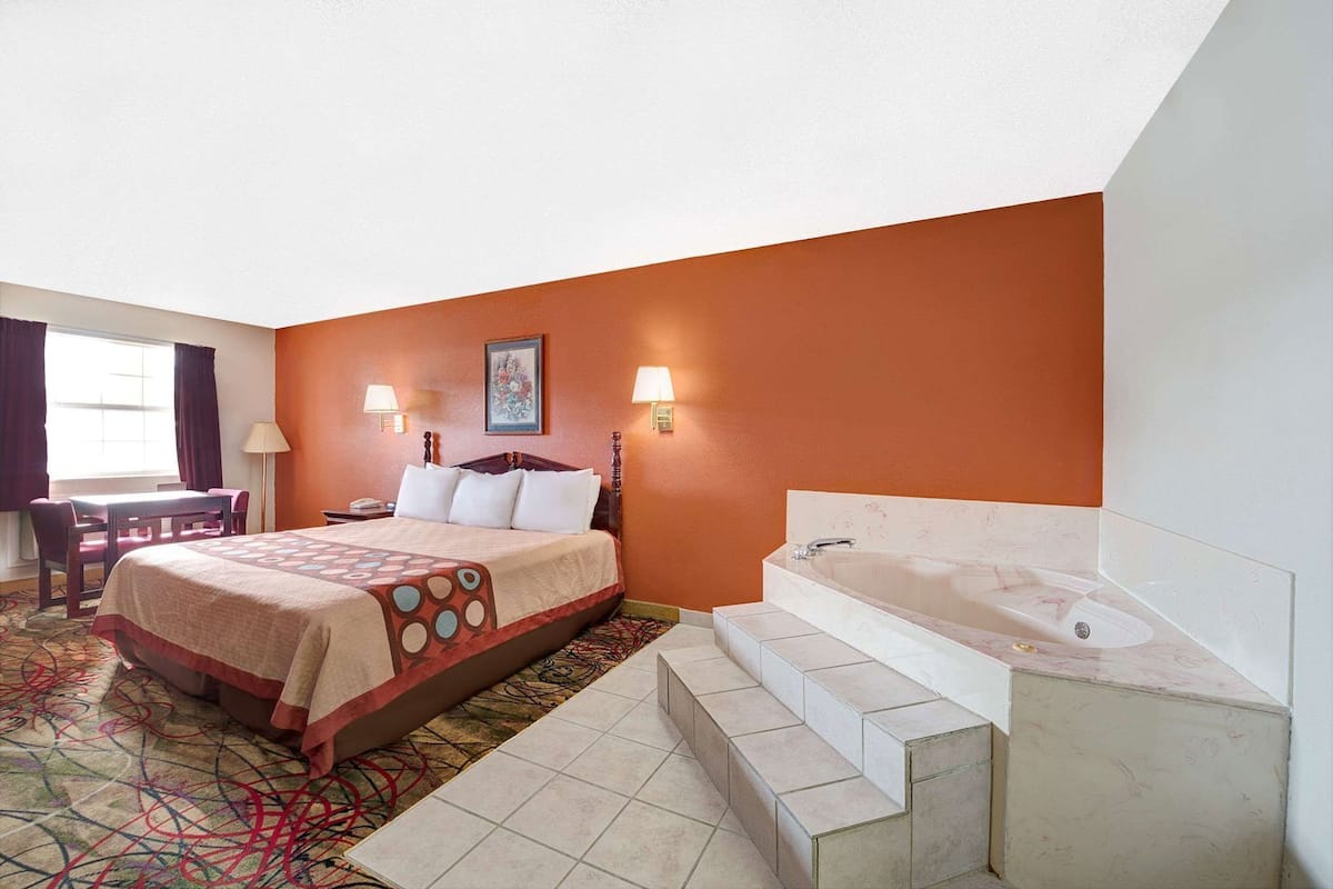 Habitación de hotel con cama, escritorio, silla y baño con bañera, además de una ventana.