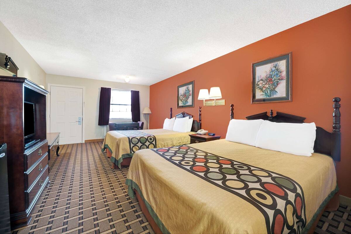 Habitación de hotel con dos camas, un aparador, un televisor y una ventana con cortinas.