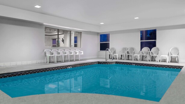Una piscina con sillas blancas alrededor, un borde de azulejos y una ventana con vistas.
