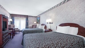 Una habitación de hotel con dos camas, un escritorio, una silla, un televisor y un cuadro en la pared.