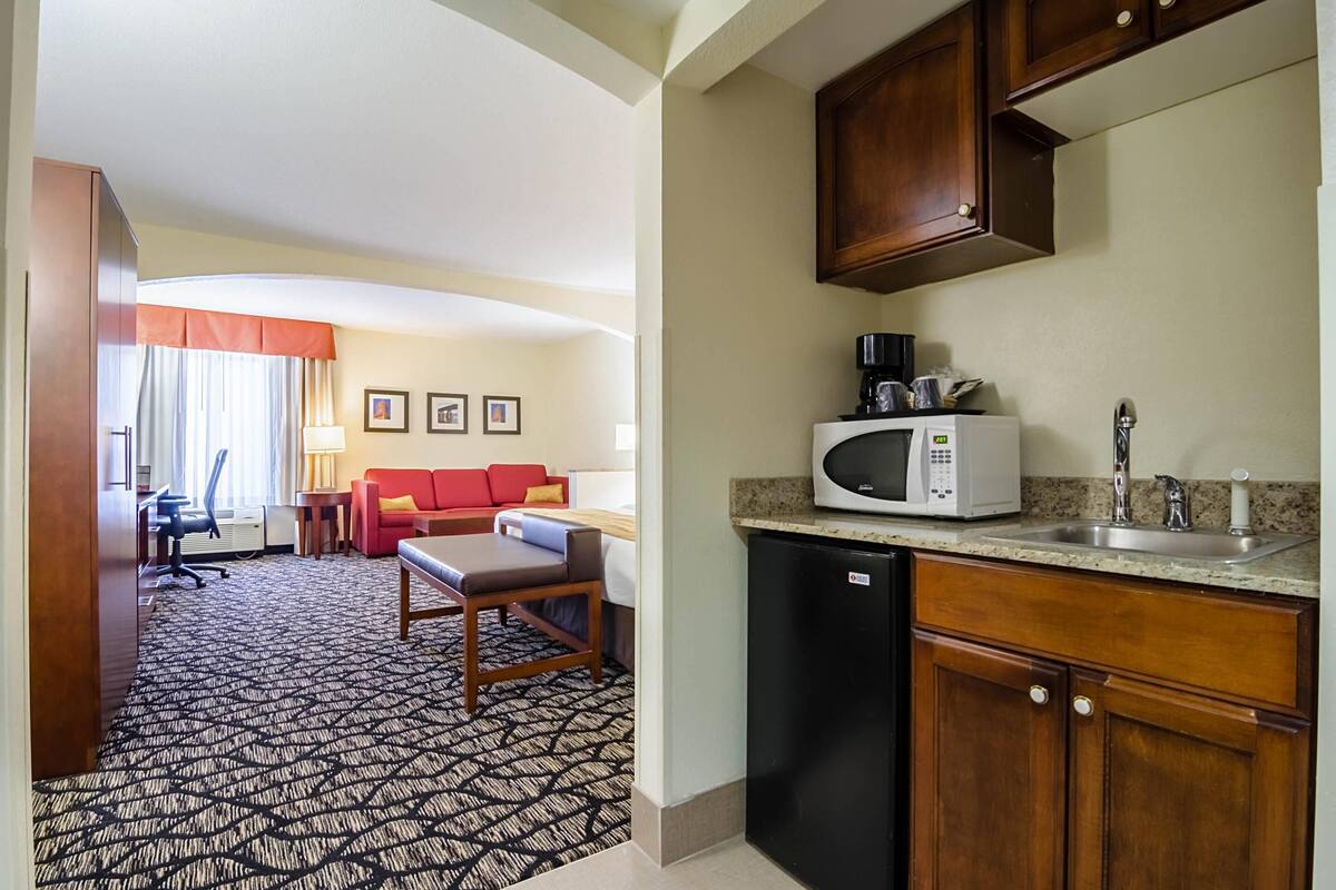 A hotel room with a kitchenette, a dining area with a red sofa, and a patterned carpet.