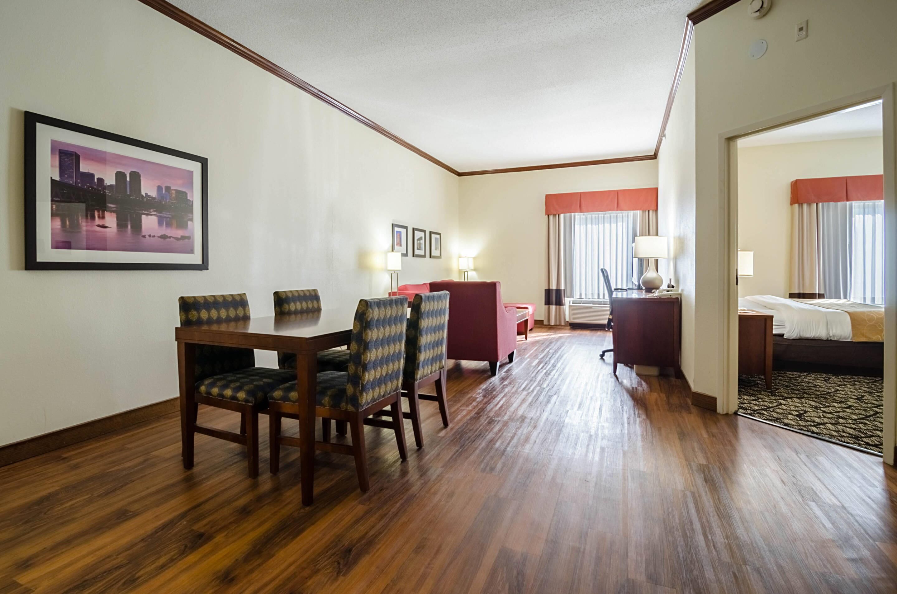 A hotel room with a dining area, a bed, a desk, and a window with curtains.