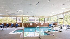 En inomhuspool med väggar av genomskinligt glas, blå solstolar och en tegelvägg med fönster.