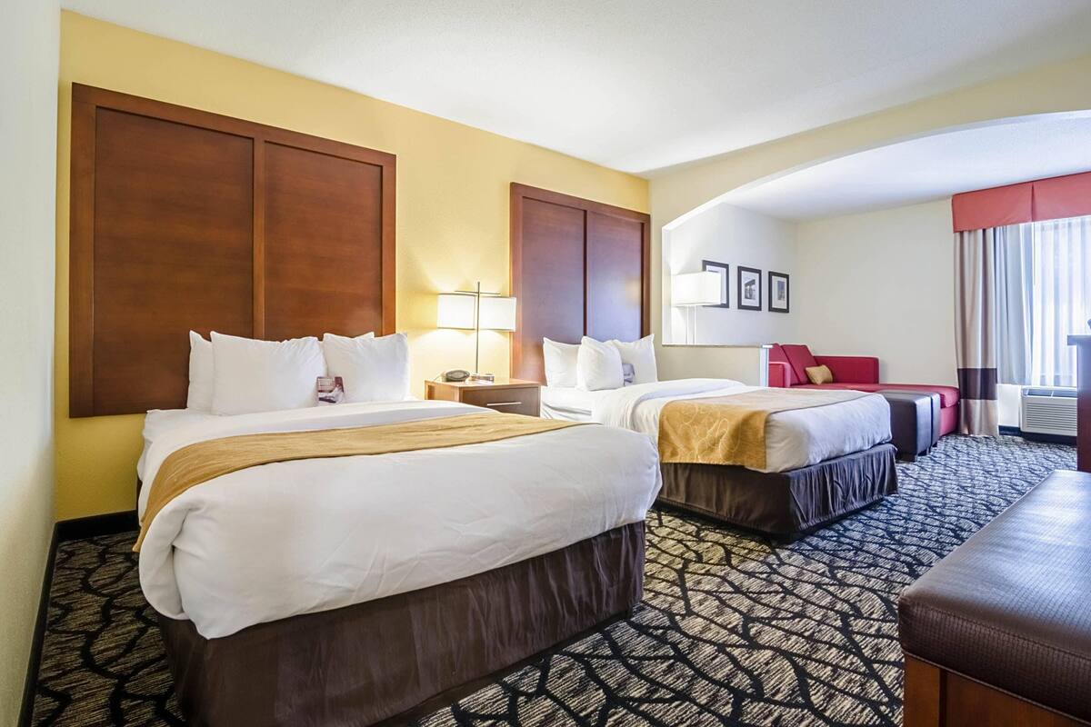 A hotel room with two beds, a desk, a chair, and a large window.