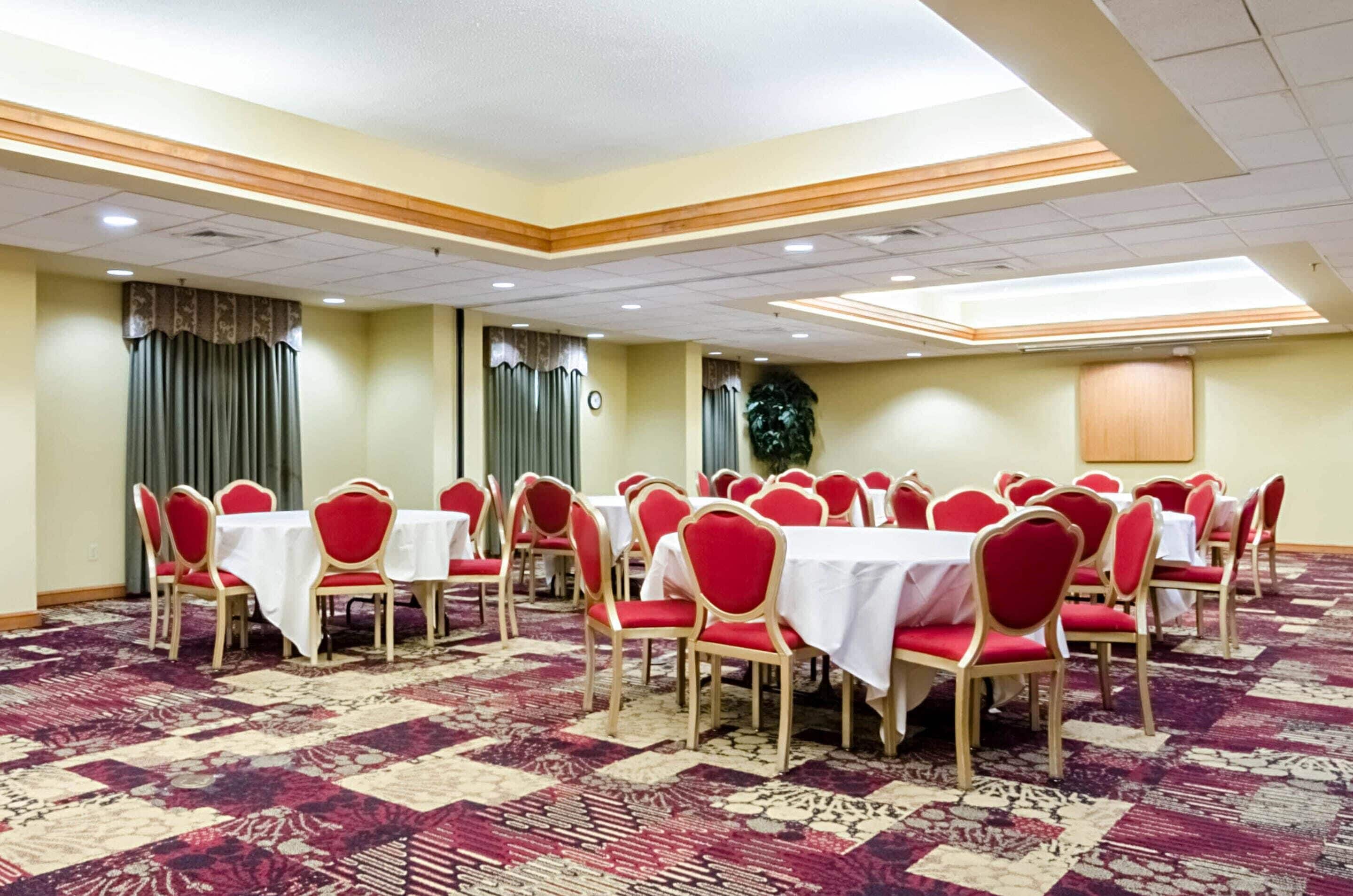 A conference room with round tables and red chairs, carpeted floor, and a wooden panel ceiling.