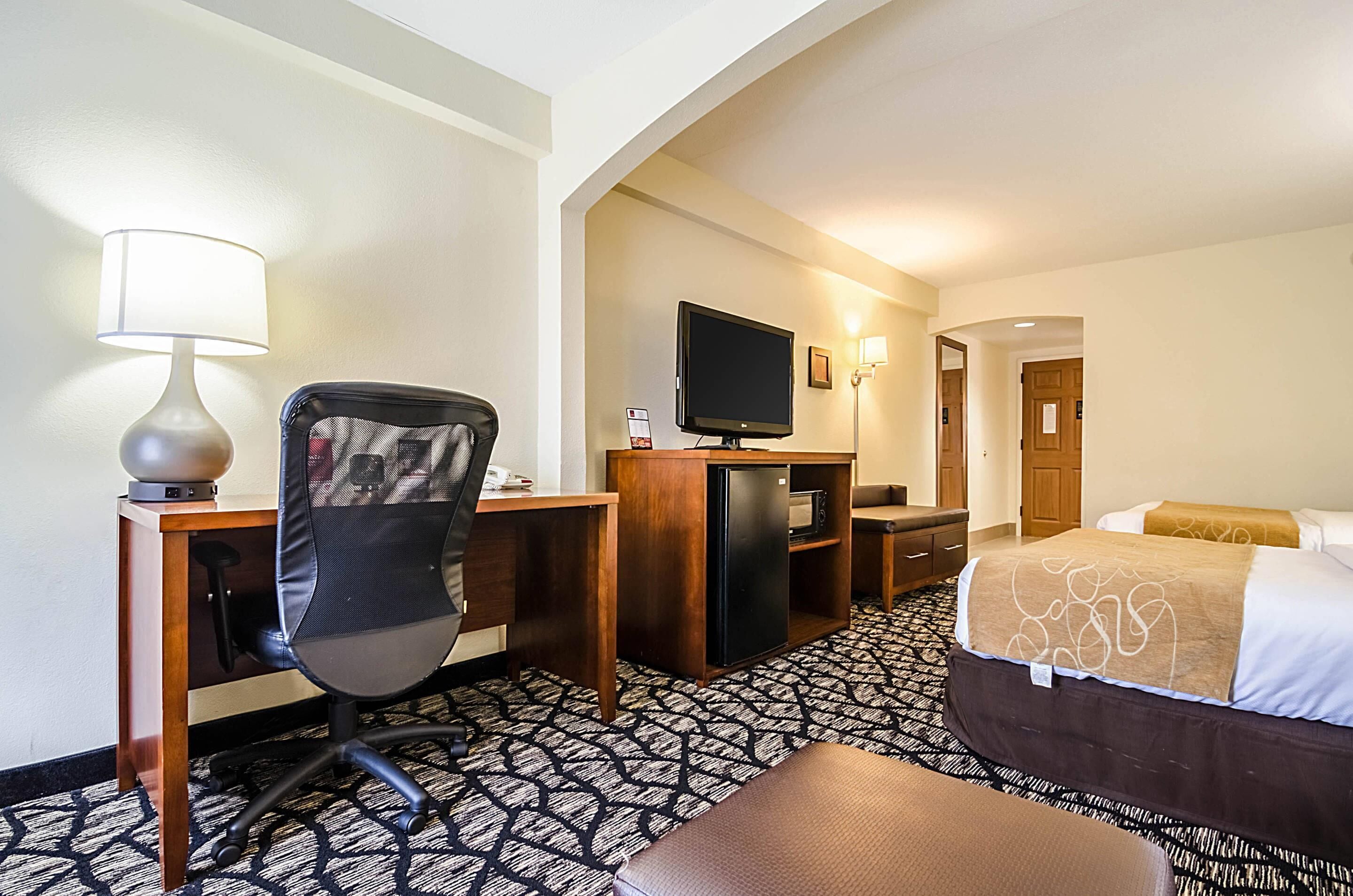 A hotel room with a desk, chair, television, bed, and a patterned carpet.