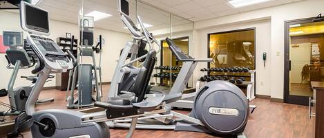 Un gimnasio con máquinas de cardio, racks de pesas y un espejo grande.