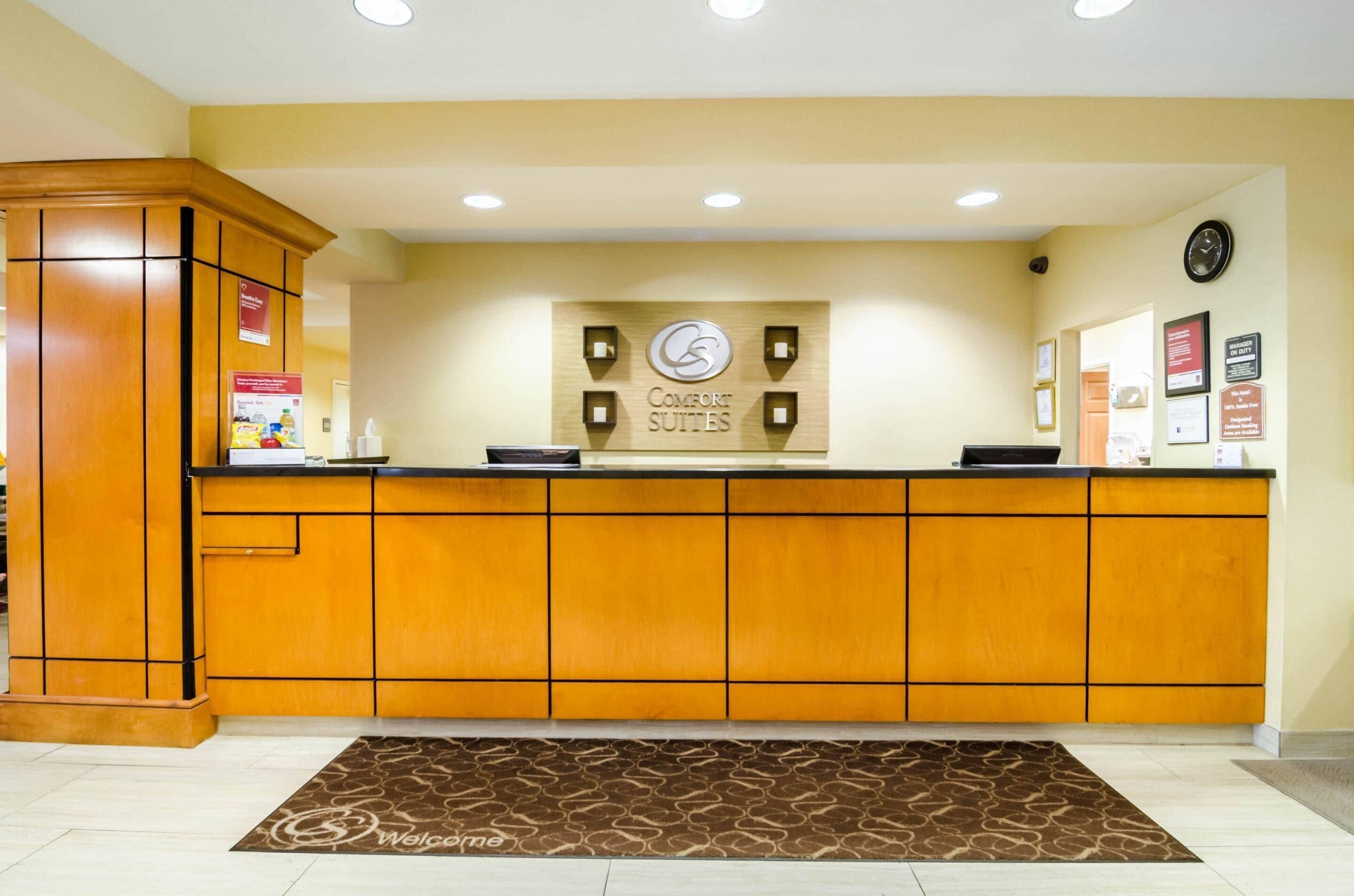 A reception desk with a 'Comfort Suites' sign, a clock, and framed notices on the wall.