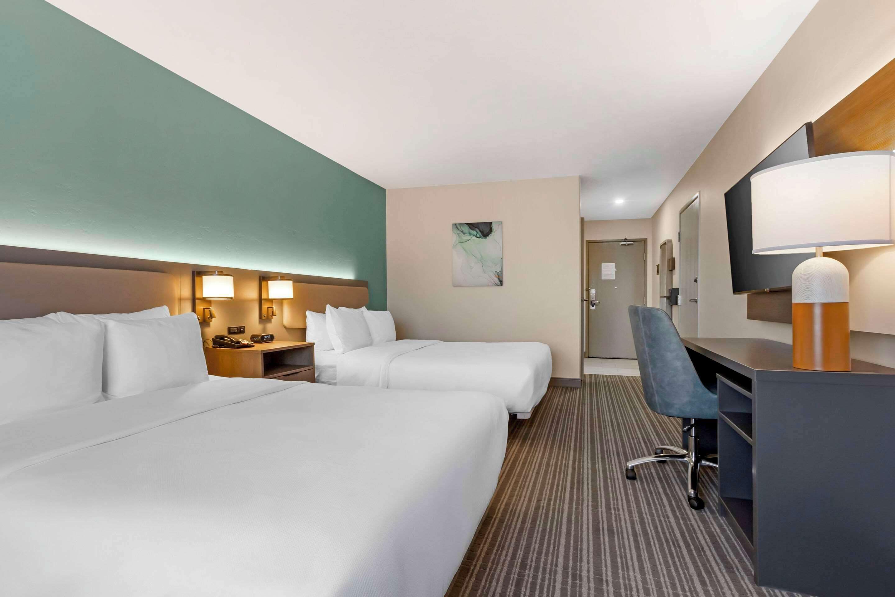 A hotel room with two beds, a desk, a chair, a TV, and a bathroom visible in the background.