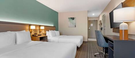 A hotel room with two beds, a desk, a chair, a TV, and a bathroom visible in the background.