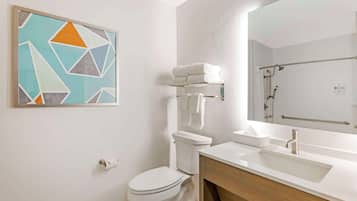 A modern bathroom with a white toilet, a sink, and a mirror. There is a towel rack with folded towels and a framed abstract painting on the wall.