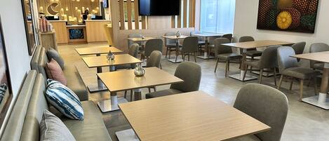 A modern restaurant with wooden tables and cushioned seating, a bar area, and a large pineapple artwork on the wall.