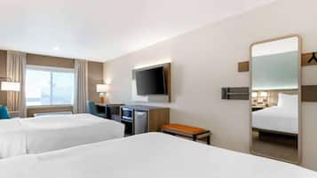 A hotel room with two beds, a desk, a television, a mirror, and a window with curtains.