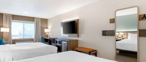 A hotel room with two beds, a desk, a television, a mirror, and a window with curtains.