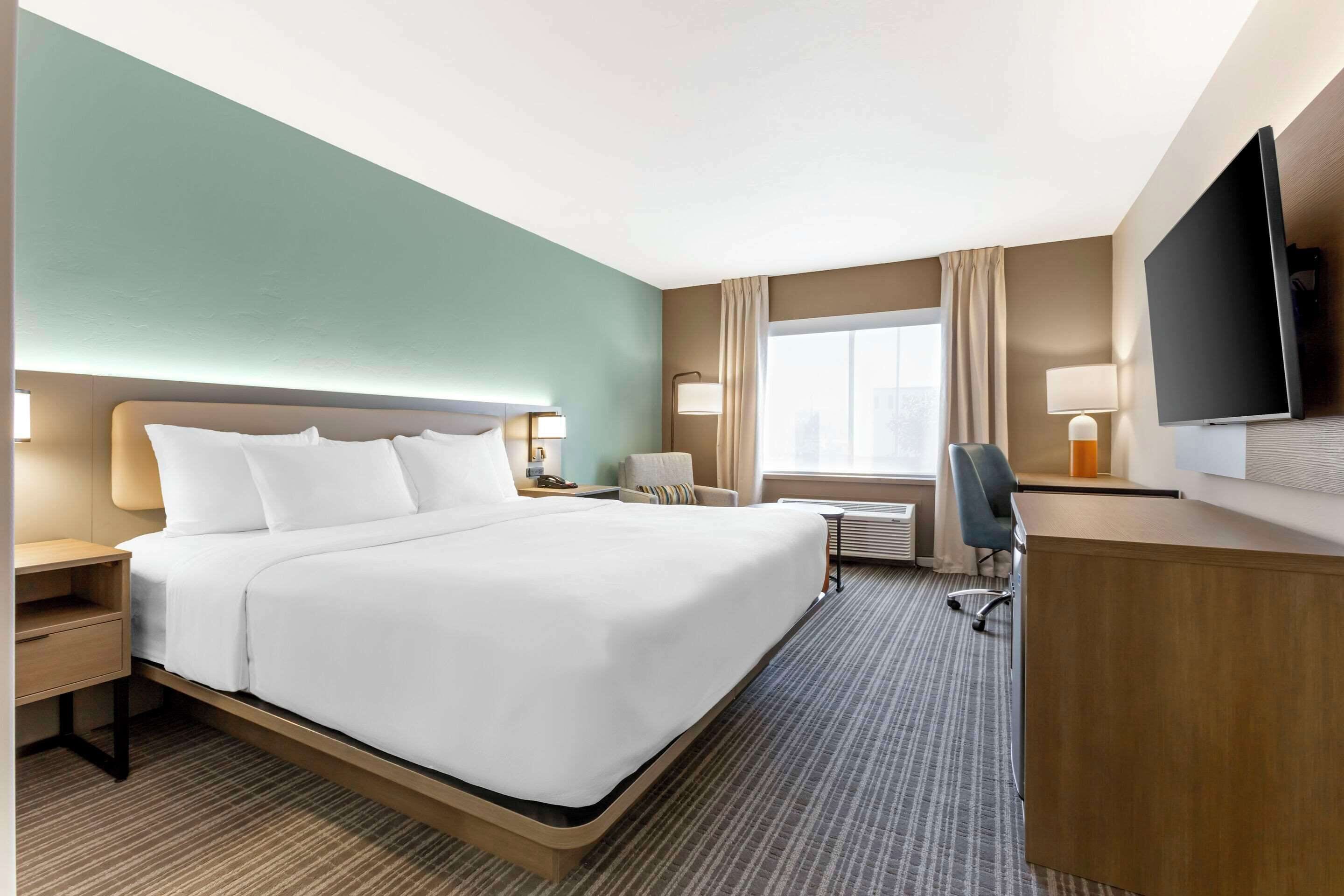 A hotel room with a large bed, a desk, a chair, a TV, and a window with curtains.
