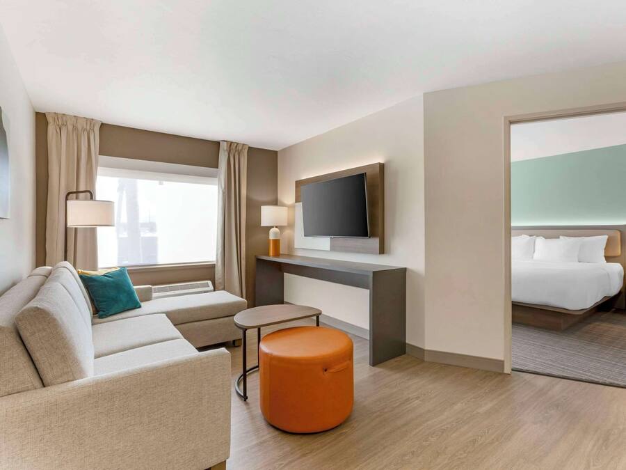 Une chambre d’hôtel équipée d’un canapé, d’un pouf, d’une télévision, d’un bureau et d’un lit.