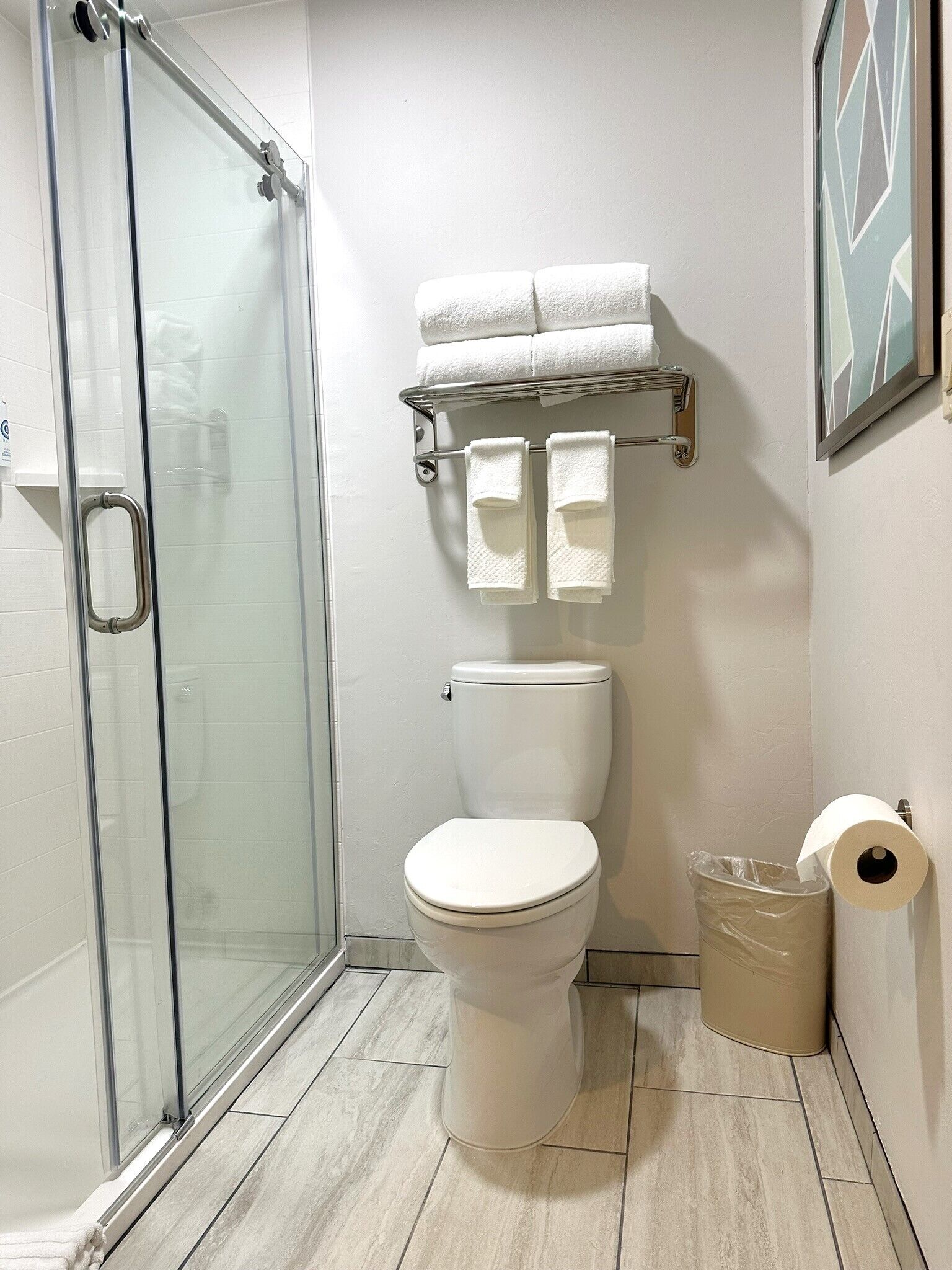 Ein Badezimmer mit Duschkabine aus Glas, Toilette, Handtuchhalter mit Handtüchern und einem Mülleimer.