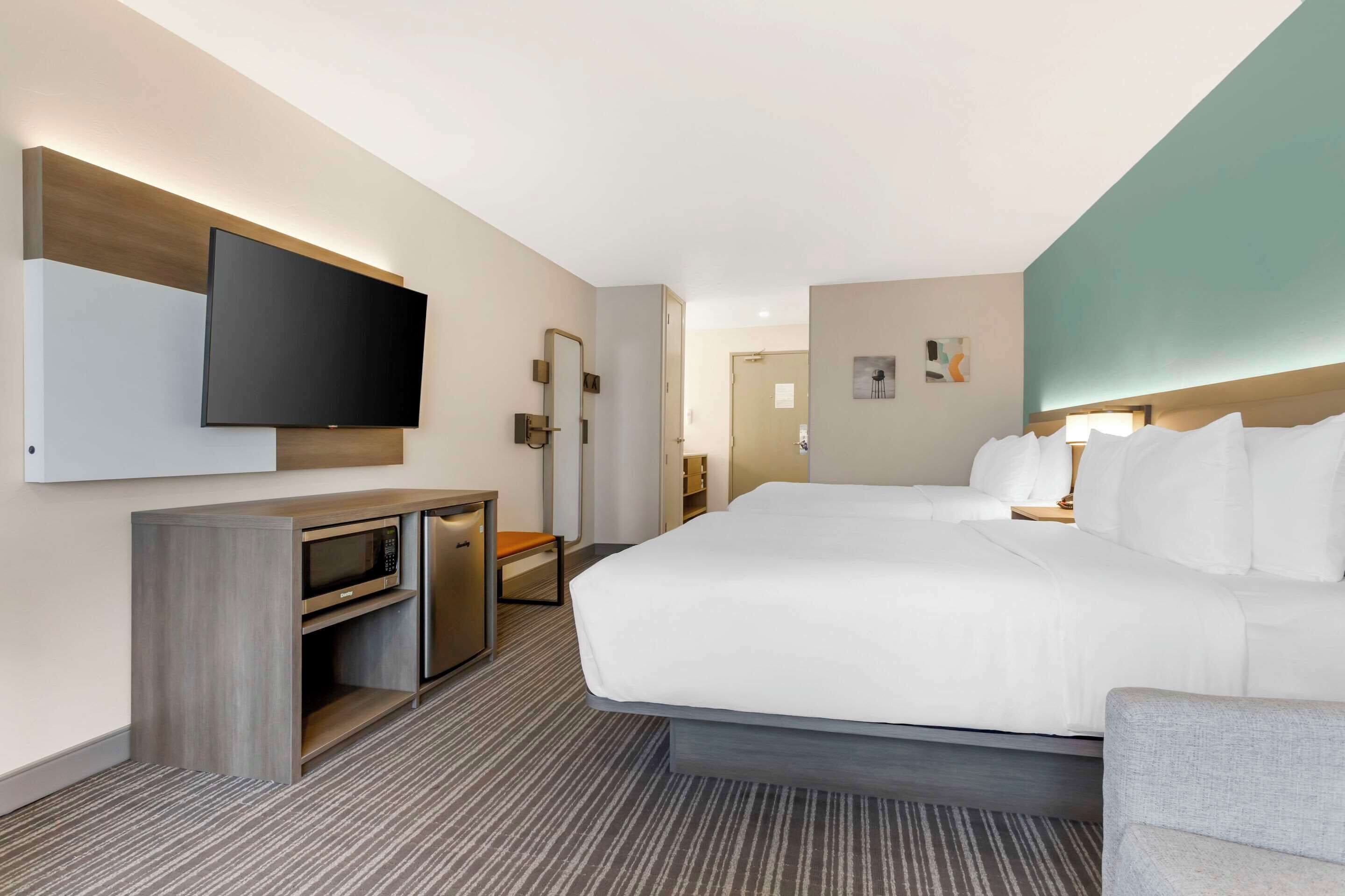 Ett modernt hotellrum med en stor säng, en platt-TV som är monterad på väggen, ett skrivbord med en mikrovågsugn och en liten sittgrupp.