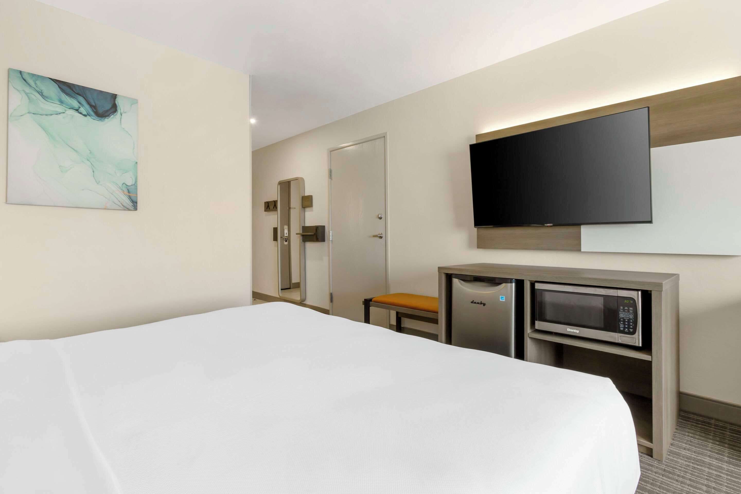 A hotel room with a bed, a desk with a microwave, a television, and a mirror.