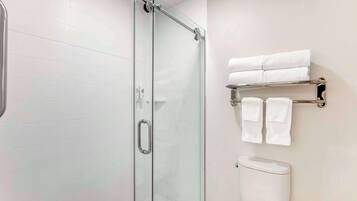 Un baño con cabina de ducha de vidrio, inodoro y toallero con toallas dobladas.