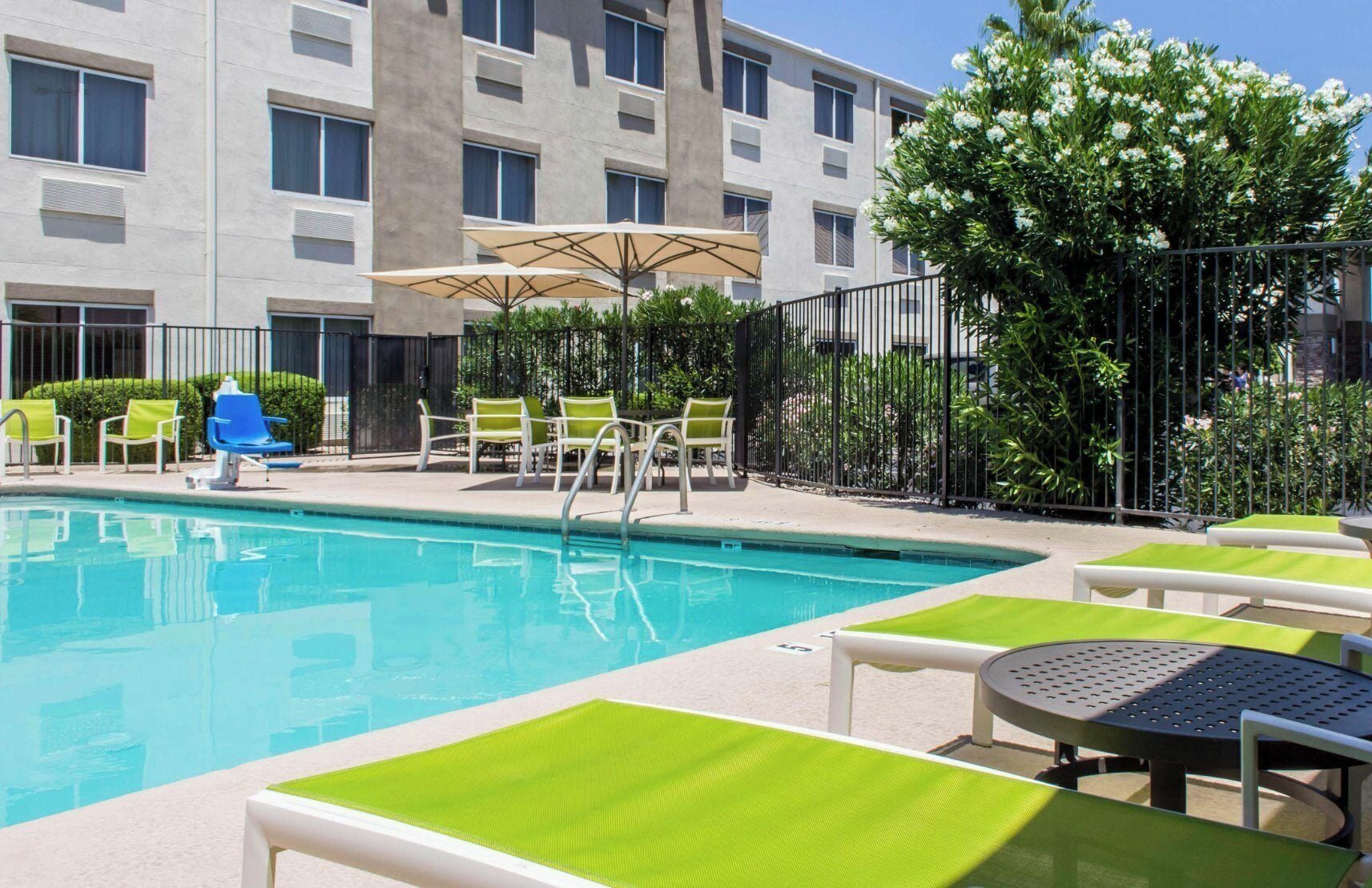 A hotel pool area with a clear pool, green lounge chairs, and umbrellas.