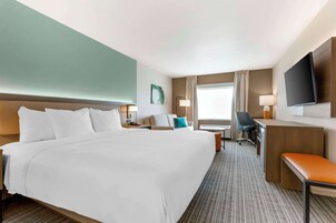 Habitación de hotel con una cama grande, un escritorio, una silla, un televisor y una ventana con cortinas.