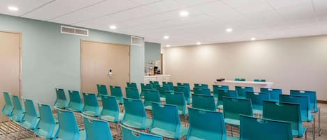 Une salle de conférence avec des rangées de chaises de couleur turquoise, une table blanche et un mur beige.